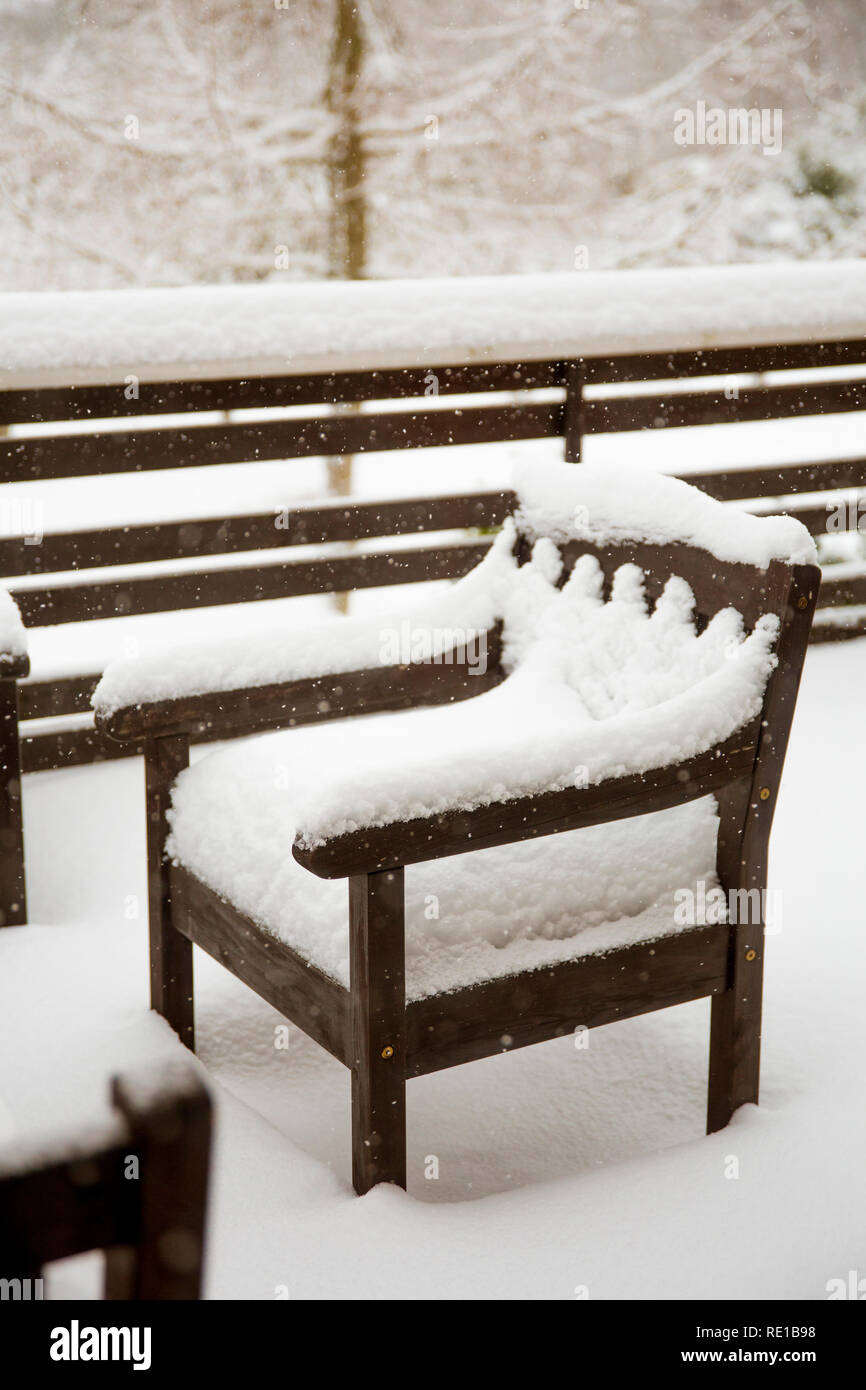 Fresh clean snow covering brown wooden Mahogany color stained garden chairs and table on home balcony. Garden furniture maintenance after cold winter Stock Photo