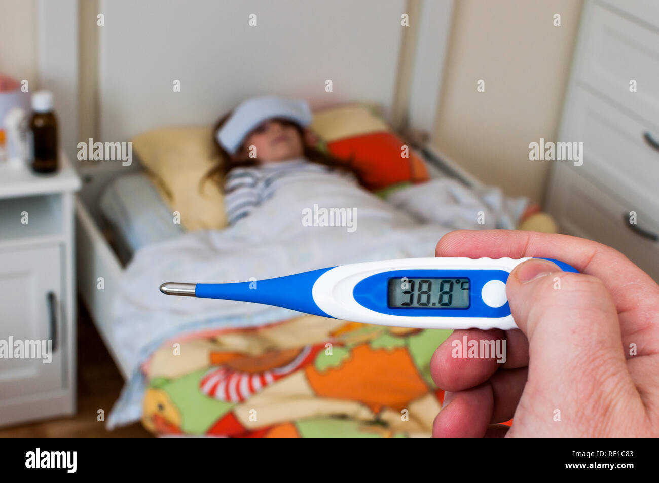 close up on a digital thermometer  that marks 38 degrees Celsius.  Little girl into bed with wet cloths on forehead Stock Photo