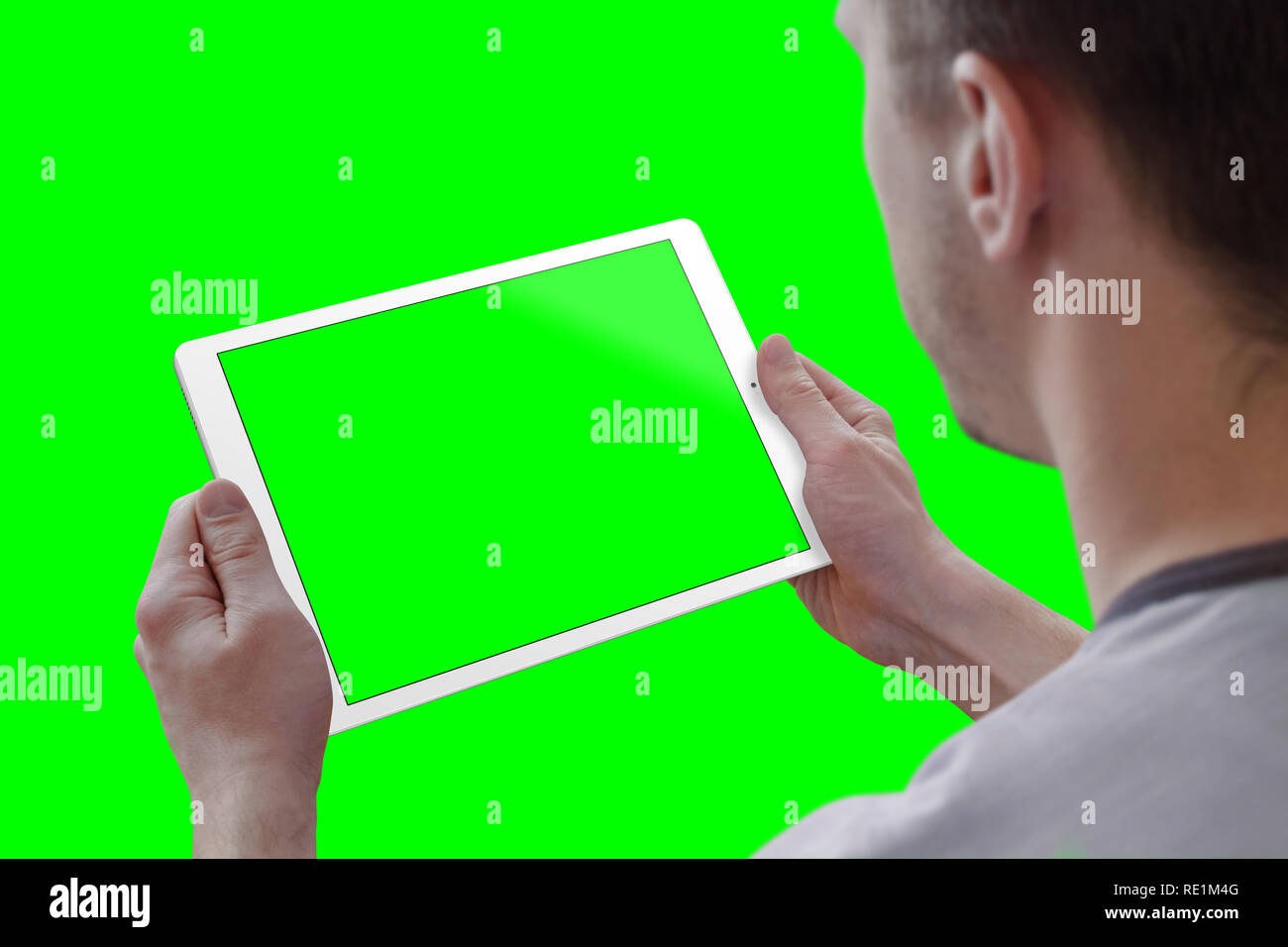 Man holding tablet in horizontal position. View over the shoulder. Isolated screen for mockup, and background in green for video editors. Stock Photo