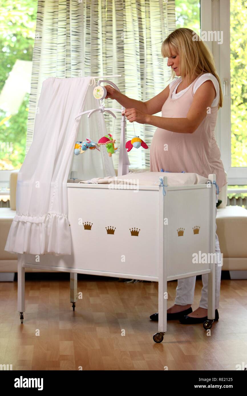 Pregnant woman, 9th month, at home, decorating the baby's cot with a mobile Stock Photo