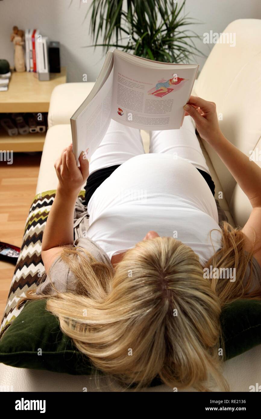 Pregnant woman, 9th month, lying on the sofa at home and reading a book