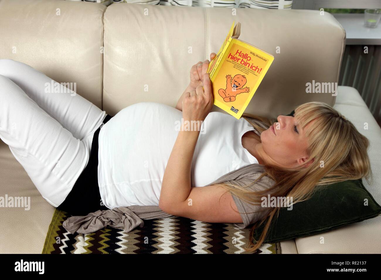 Pregnant woman, 9th month, lying on the sofa at home and reading a book