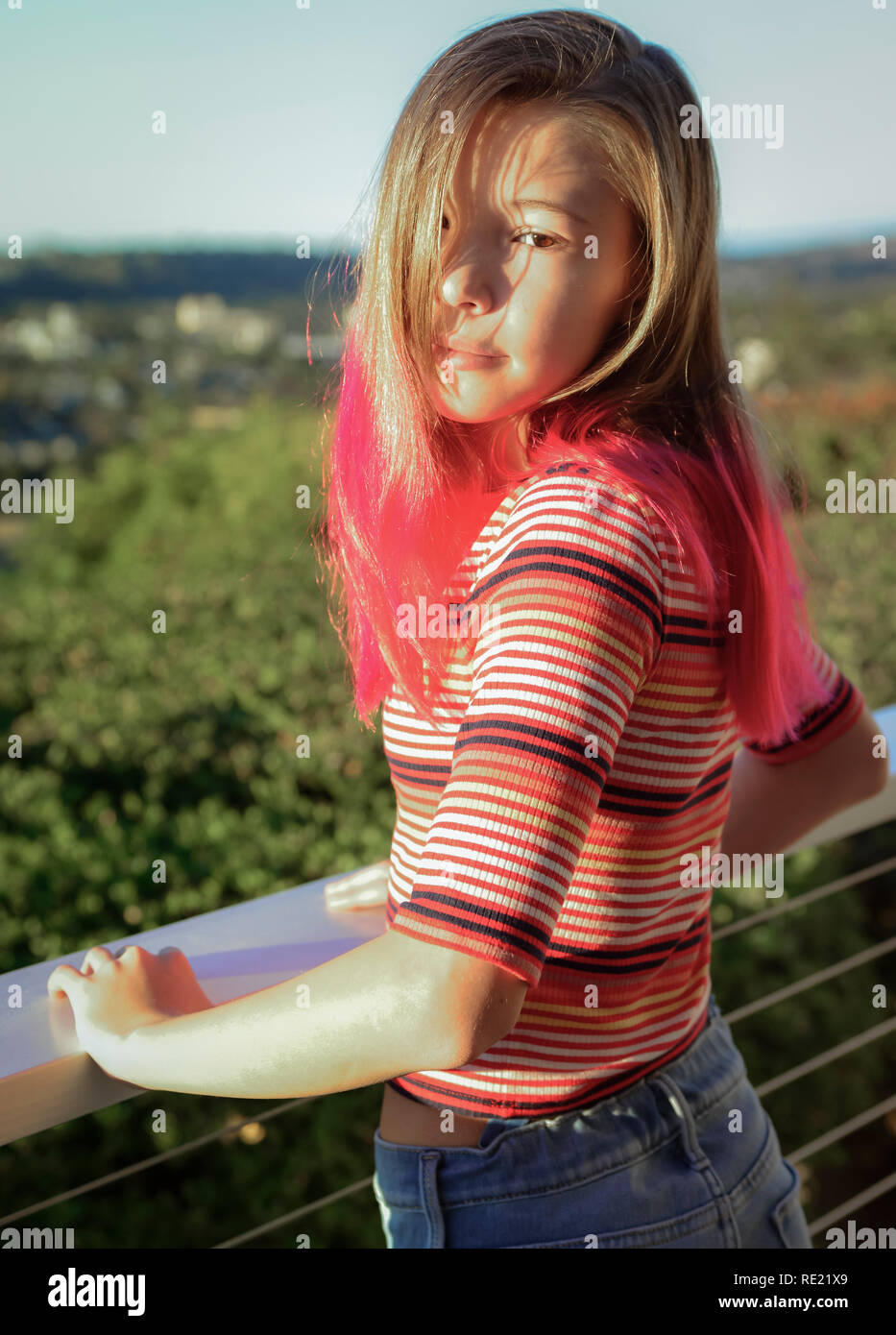 Tween girl with trendy dip dyed pink hair and with her eyes staring out emotionlessly outside on balcony Stock Photo