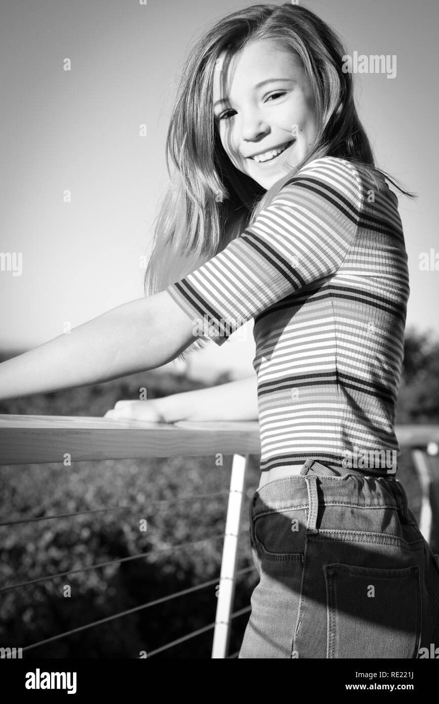 Happy tween smiles while bracing herself on balcony outside in black and white Stock Photo
