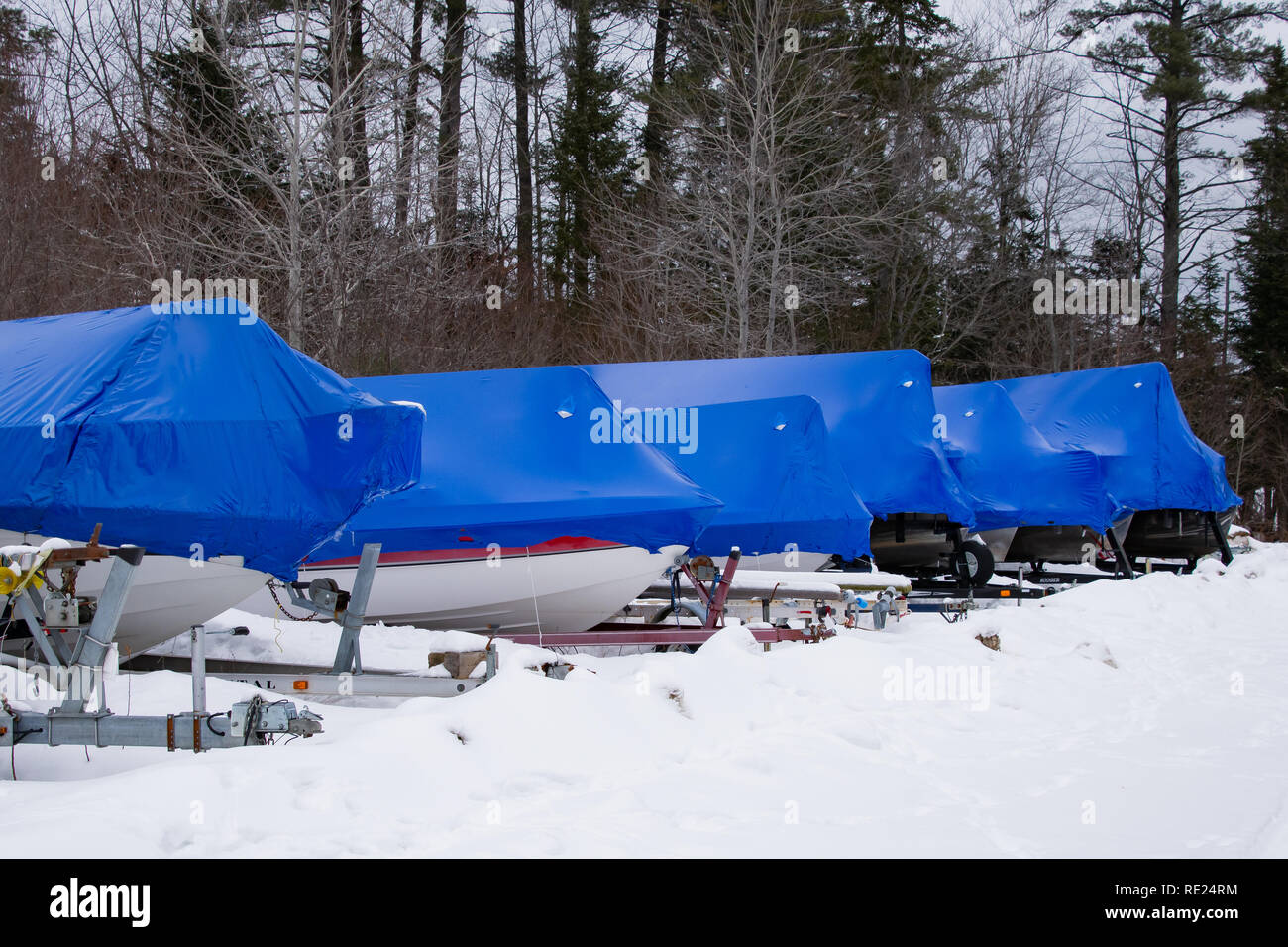A row of boats sitting on trailers in the snow covered with blue polymer plastic film shrink wrap for protection in Speculator, NY USA Stock Photo