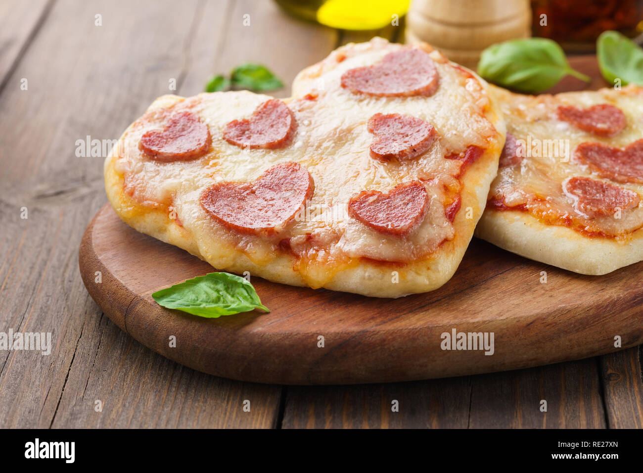 Mini pizzas - Fresh homemade heart shaped mini pizzas with pepperoni, cheese, tomatoes and basil. Wooden board. Stock Photo