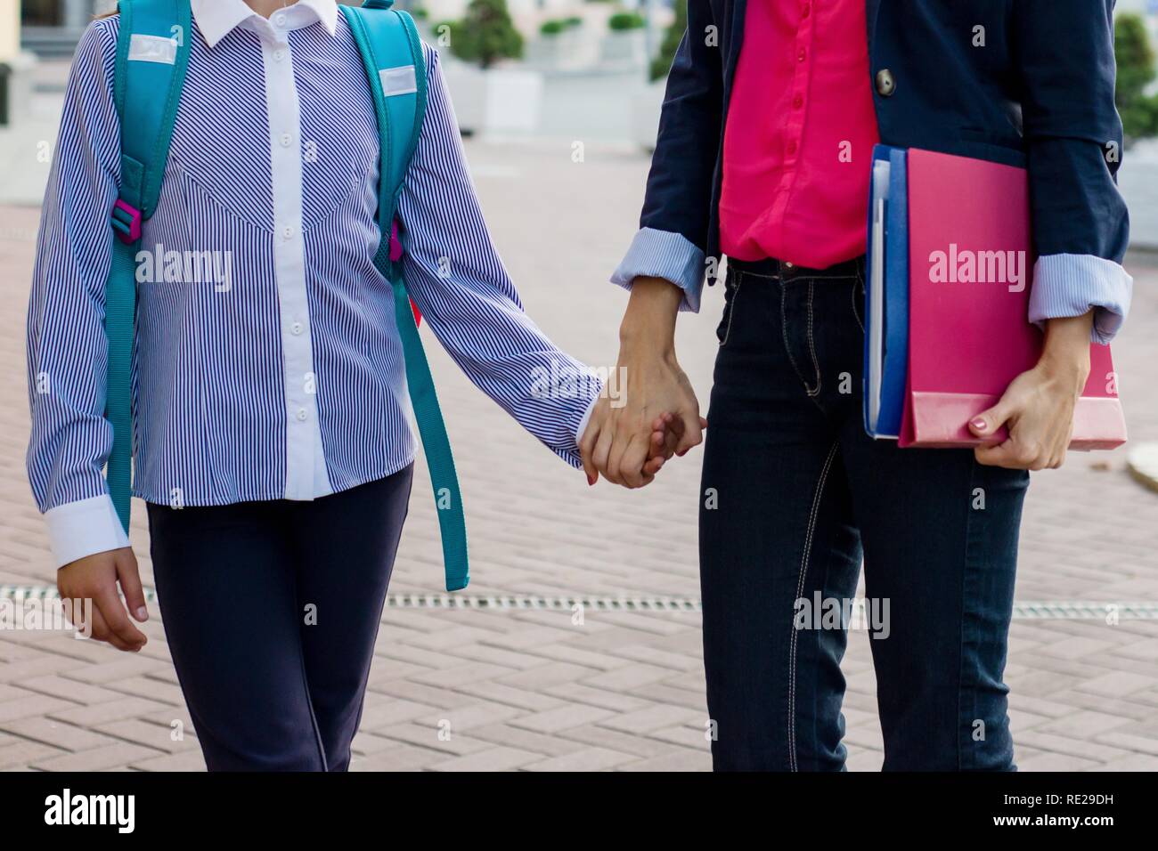 Woman teacher and girl student holding hands, outdoor background Stock Photo