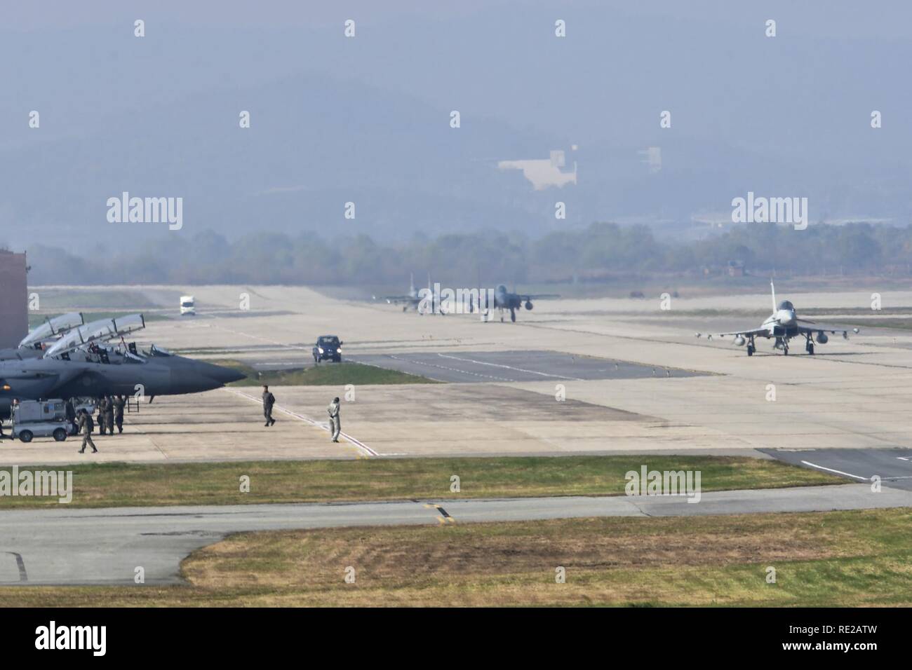 A United Kingdom Royal Typhoon FGR4 taxis down the runway as Republic of Korea Air Force F-15K Slam Eagle crews perform shutdown procedures during Invincible Shield on Osan Air Base, Republic of Korea, Nov. 8, 2016. Invincible Shield is an exercise intended to bolster the strong partnership between the ROK, the United States and the United Kingdom while improving combat capability in the Pacific region. Stock Photo