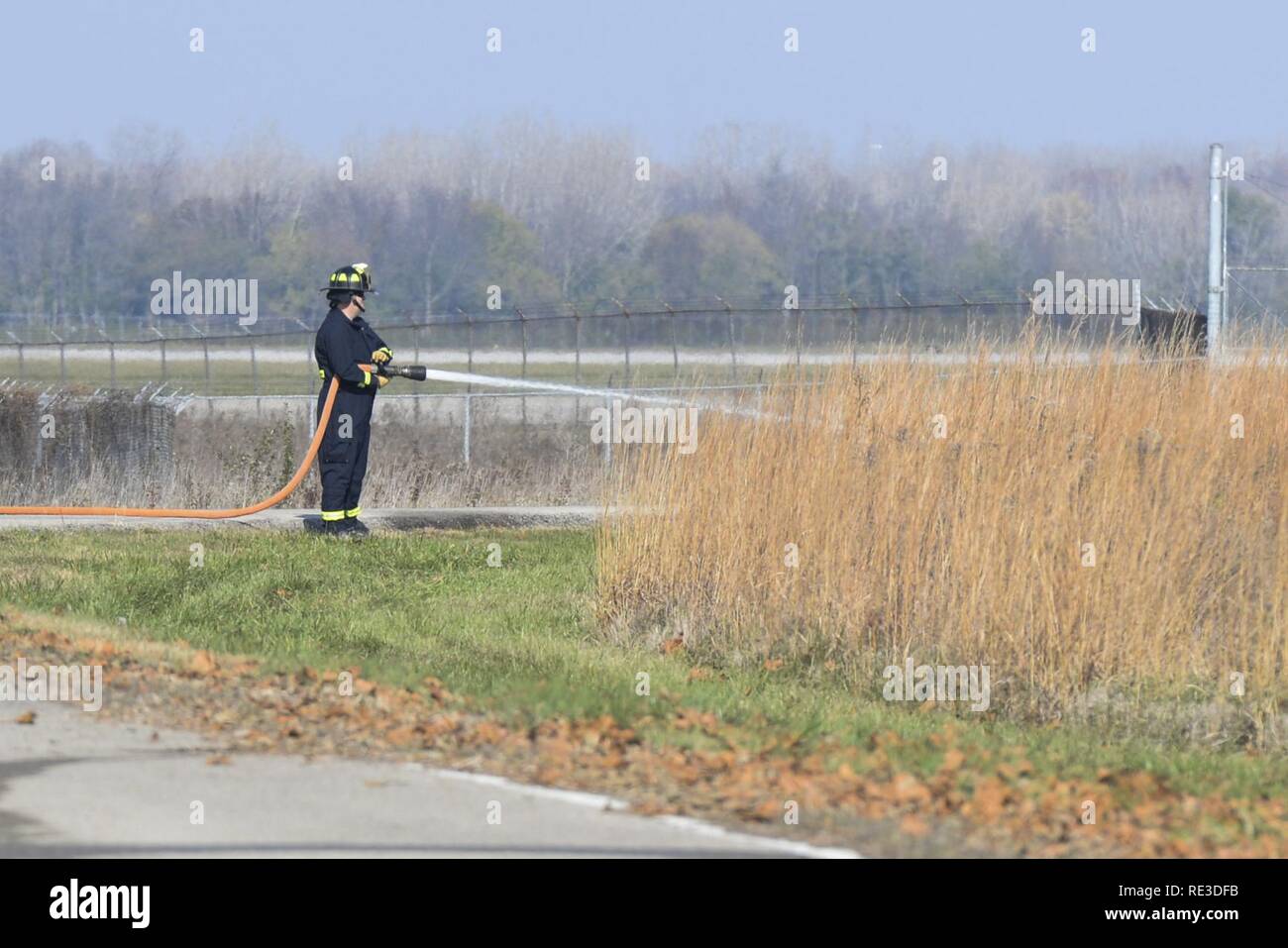 A firefighter from the 788th Civil Engineer Squadron hoses down the perimeter of a vegetation prior to the start of a controlled burn at Huffman Prairie, Wright-Patterson Air Force Base, Ohio, Nov 16, 2016. Controlled burns are needed to restore the prairie to its original character and rid it of non-native plant species. Stock Photo