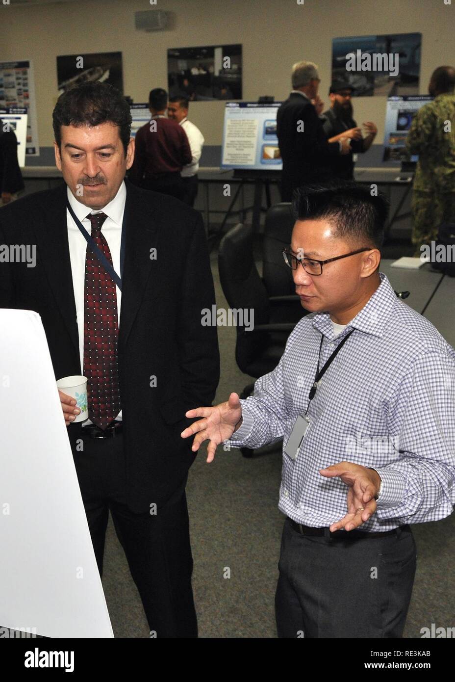 PORT HUENEME, Calif. - Naval Facilities Engineering and Expeditionary Warfare Center (NAVFAC EXWC) Technical Director, Kail Macias (left) talks with Man Nguyen, an engineer and Principle Investigator with Naval Surface Warfare Center, Port Hueneme Division (NSWC PHD) during a joint end of year showcase for the Naval Innovative Science and Engineering (NISE) Program. U.S. Navy Stock Photo