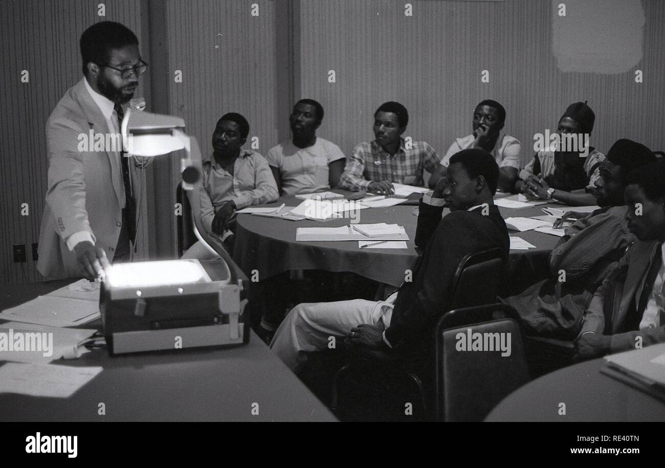 Man speaking to a group of men in a classroom; putting a document on a