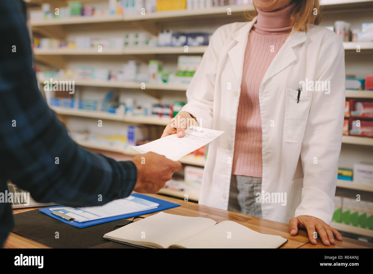 Customer handing over a medical prescription to the female chemist standing behind counter. Female apothecary taking prescription from customer at dru Stock Photo