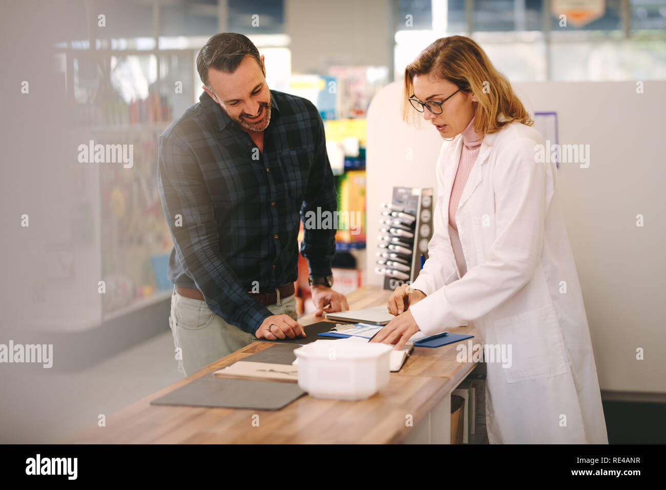 Female pharmacist explains a prescription to customer. Chemist assisting a customer standing at the counter. Stock Photo