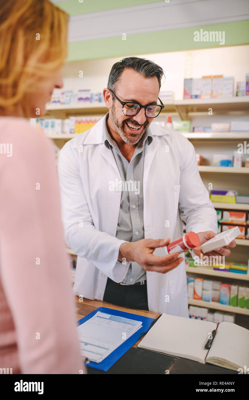 Chemist suggesting medical drug to buyer in pharmacy drugstore. Professional male pharmacist showing medicine to female customer in pharmacy. Stock Photo