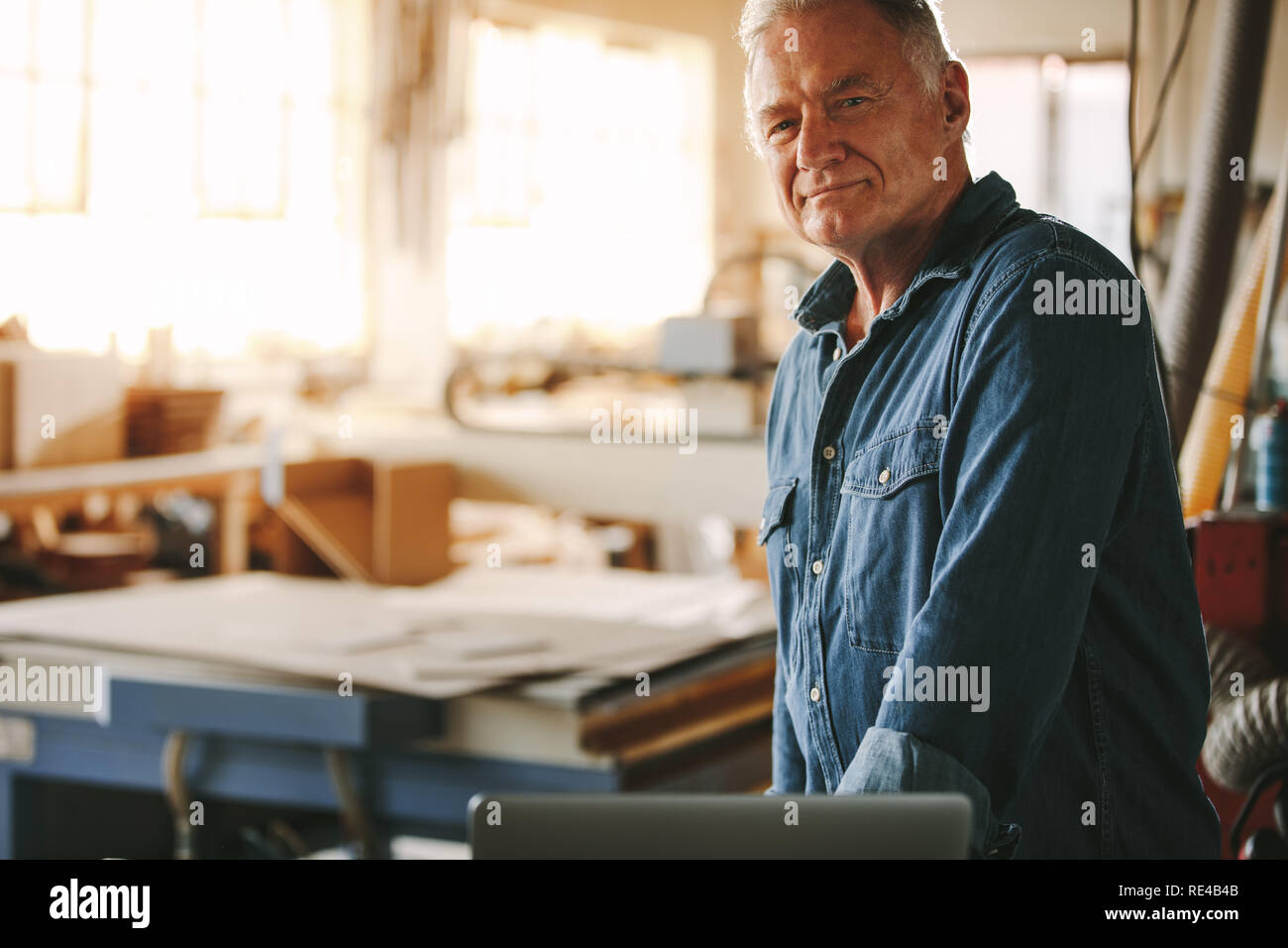 Portrait of confident senior male carpenter standing in his workshop. Mature male carpenter looking at camera. Stock Photo