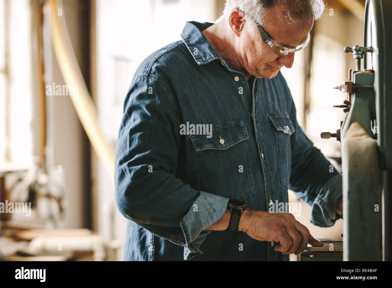 Mature male carpentry worker working in his workshop. Carpenter cutting wood on band saw machine at workshop. Stock Photo
