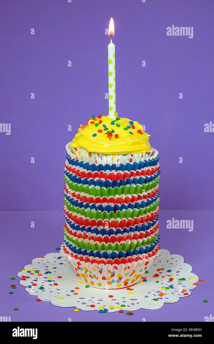 cupcake with polka dot candle in stack of colorful paper liners on white paper lace doily Stock Photo