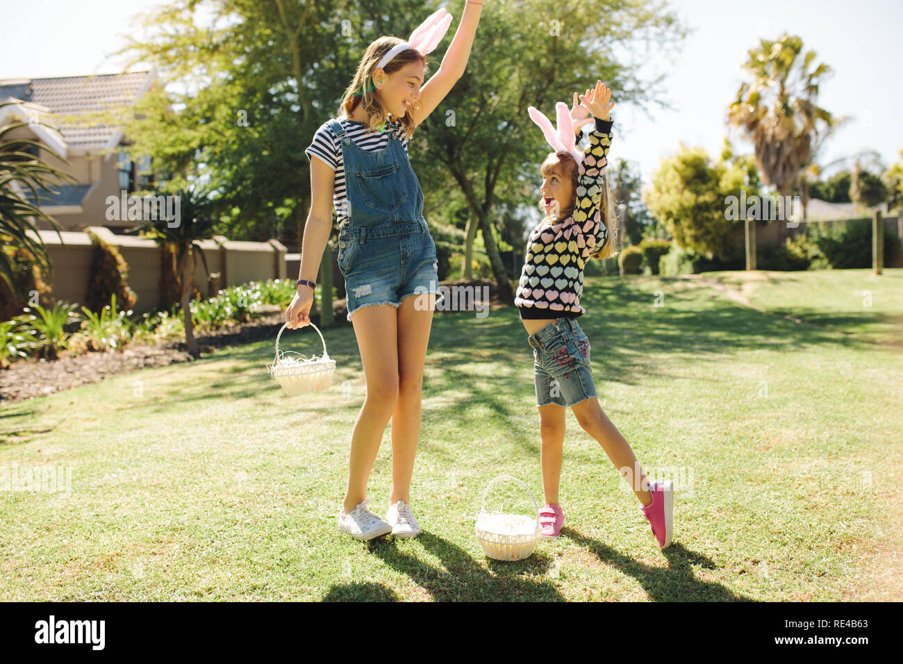 Two girls wearing rabbit ear headband and playing outdoors. Girls playing in their backyard with baskets. Stock Photo