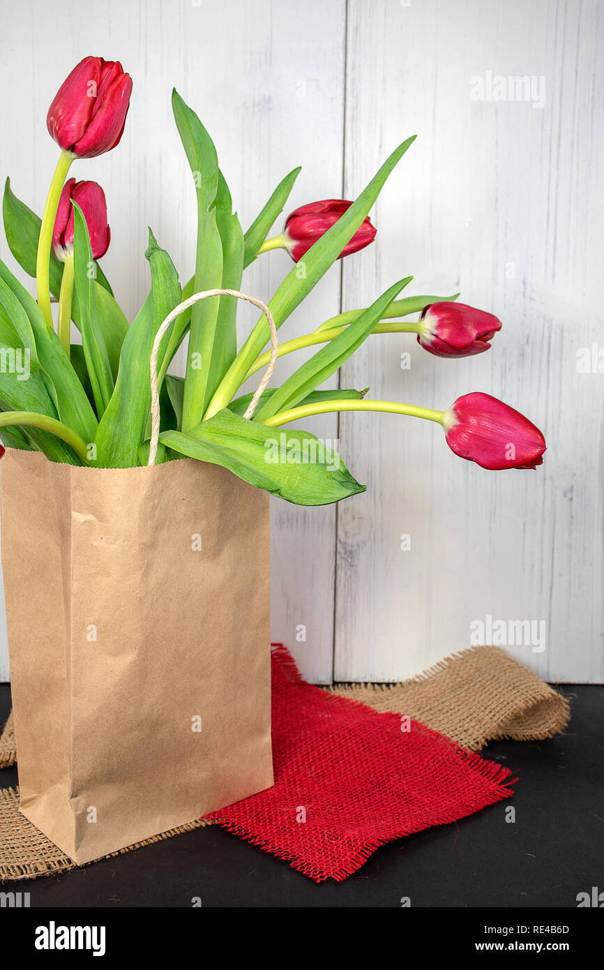 red tulips in generic paper bag on burlap fabric pieces with whitewashed wood background Stock Photo