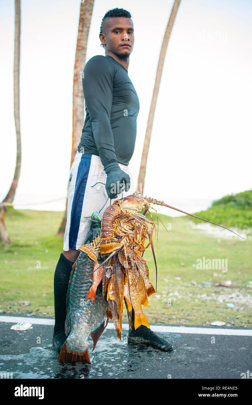 Unknown latino man proudly holding his catch: fresh lobster and giant fish. Environmental portrait, editorial use. San Andrés, Colombia. Oct 2018 Stock Photo