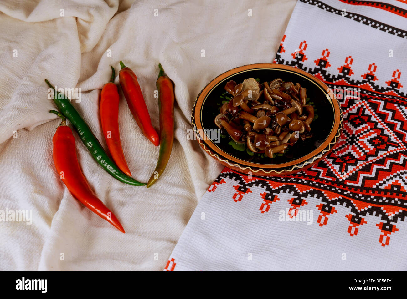 Dish from pickled mushrooms, red bitter pepper on the table, Ukrainian embroidered towel Stock Photo