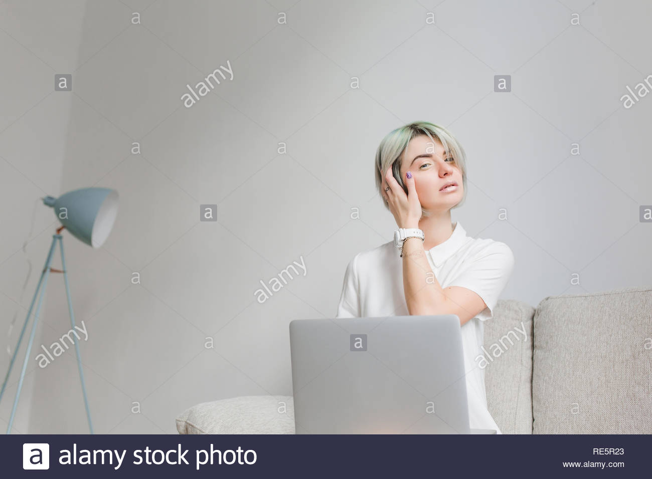 Cute Girl With Short Hairstyle Is Sitting On Sofa In Gray Studio
