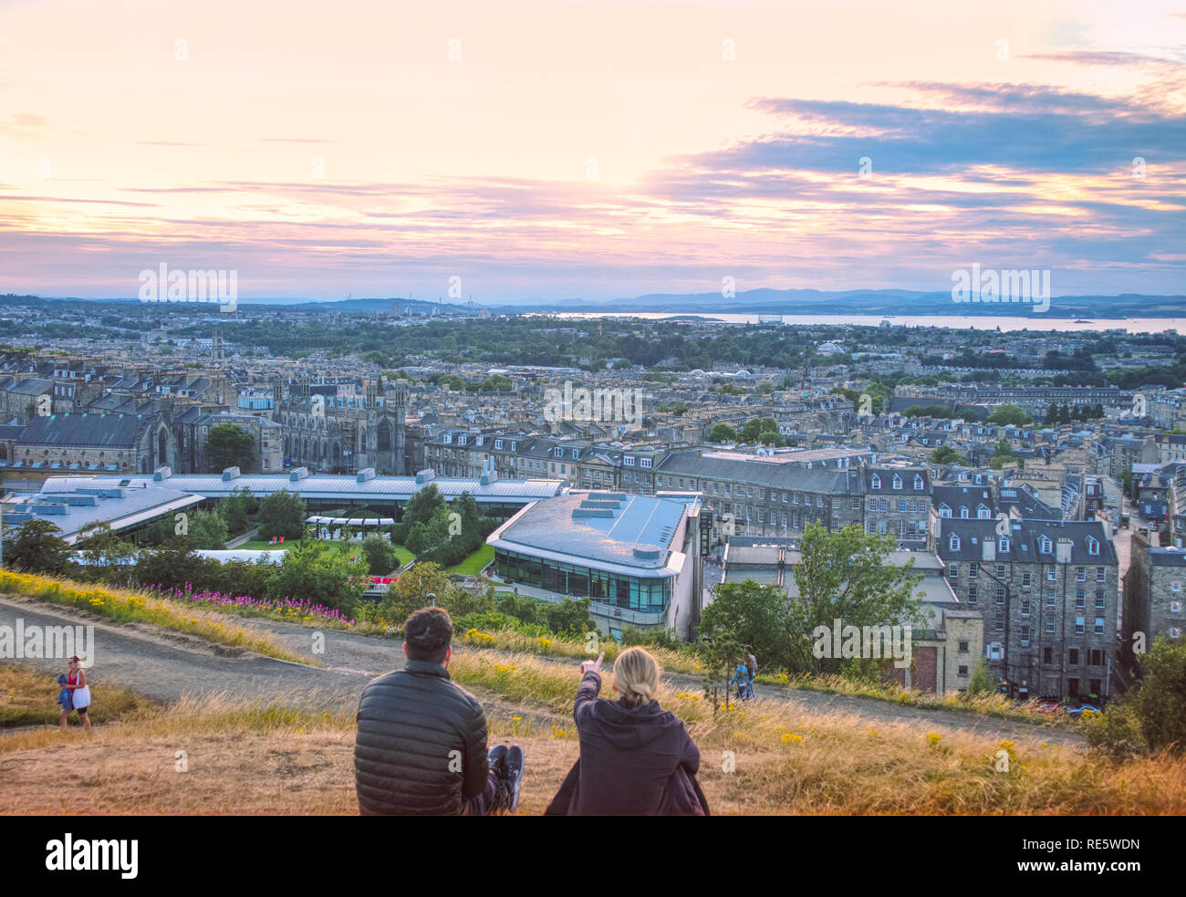 A young woman is showing her male friend a beautiful sunset over the city of Edinburgh from the famous Calton Hill. Stock Photo