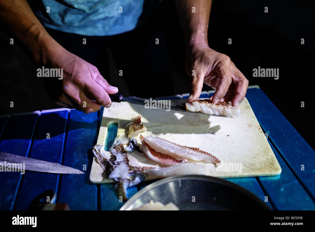 Close up of cooks hands slicing freshly caught fish for dinner on tropical beach, Iriomote, Japan Stock Photo