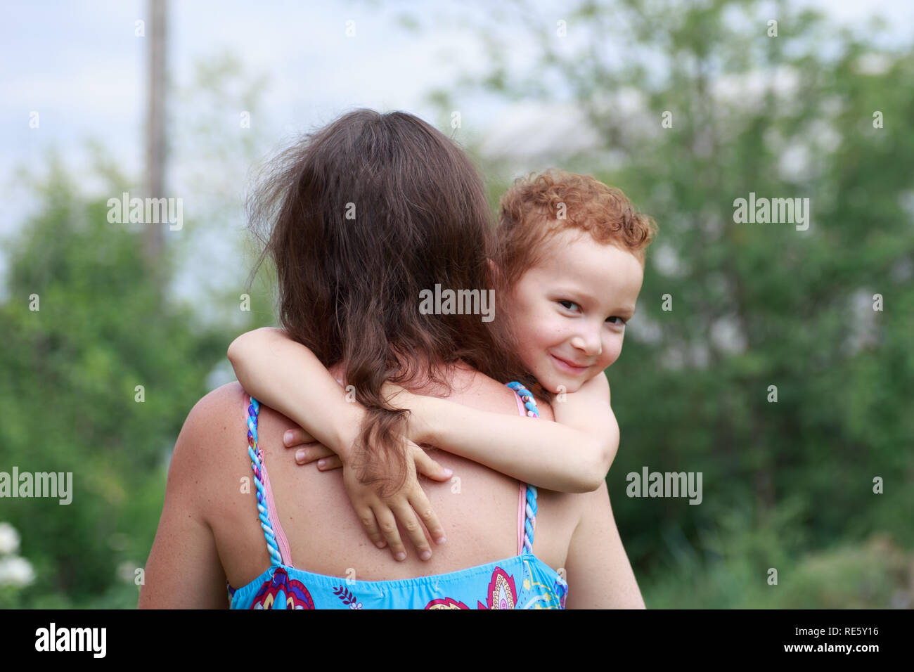portrait of funny redhead boy with freckles hugs his mom around the neck. Stock Photo