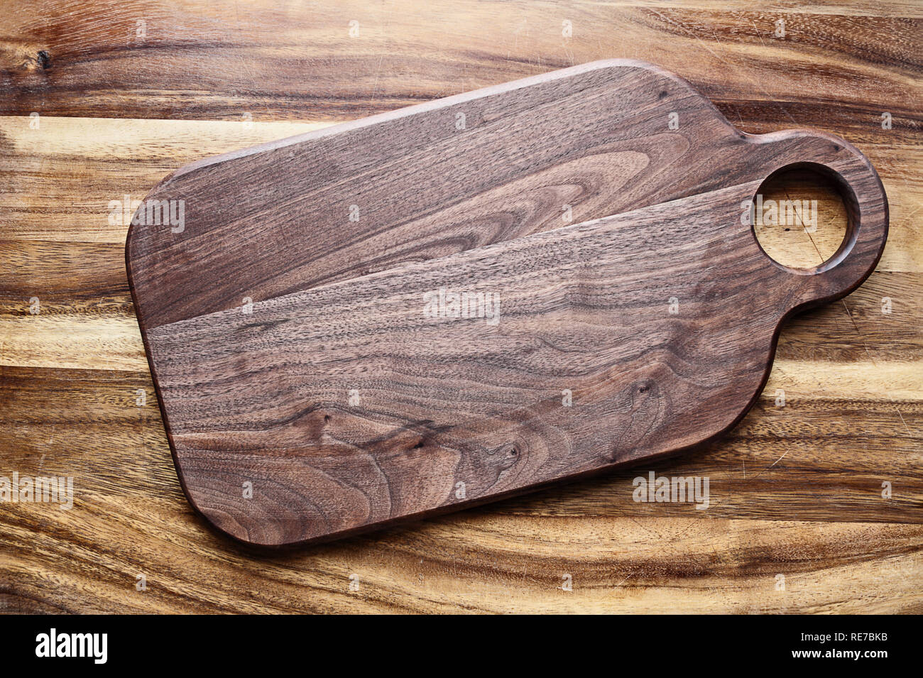 https://c8.alamy.com/comp/RE7BKB/walnut-wooden-cutting-board-with-round-handle-hold-over-oak-table-top-image-shot-from-above-in-flat-lay-position-RE7BKB.jpg