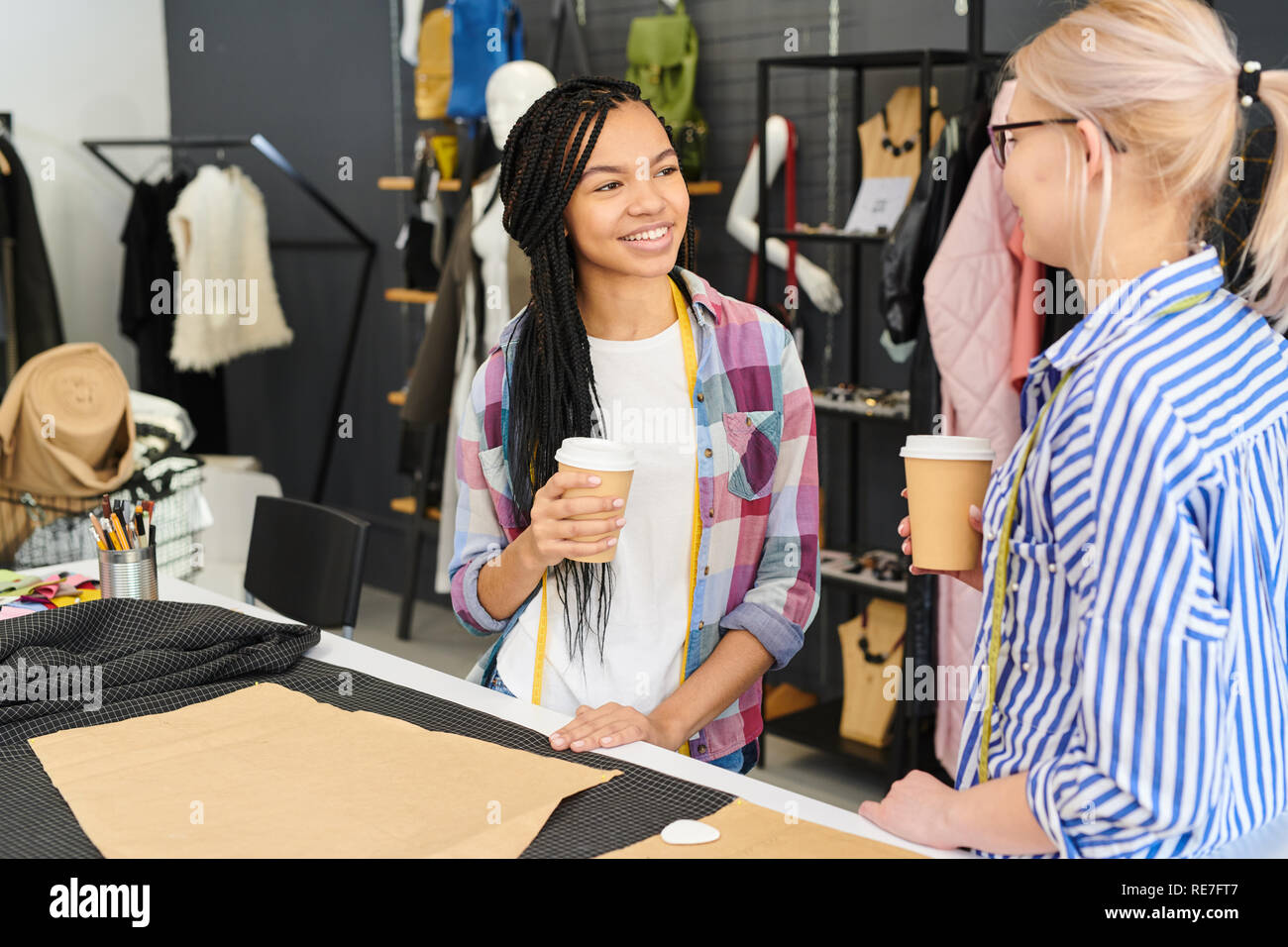 Two young women working as fashion designers in workshop, they drinking ...
