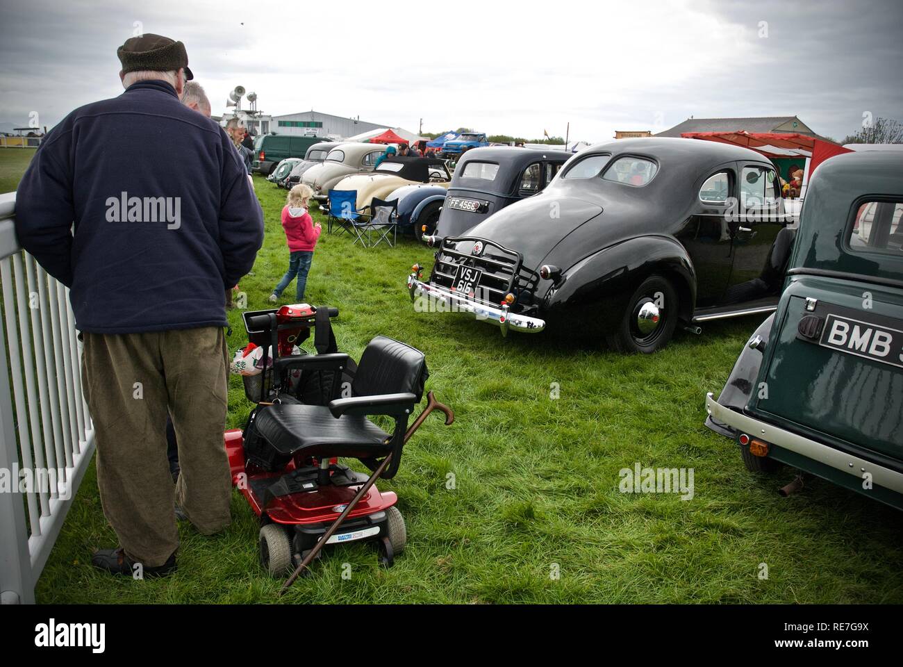 A visitor with a mobility scooter watches American car exhibits at the Anglesey Vintage Rally, Anglesey, North Wales, UK, May 2015 Stock Photo