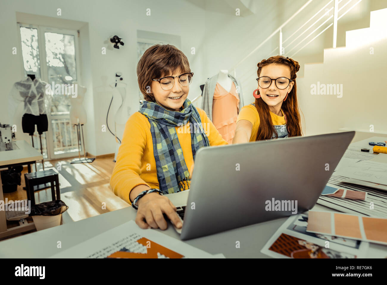 Dark-haired boy wearing yellow sweater and blue scarf using laptop Stock Photo