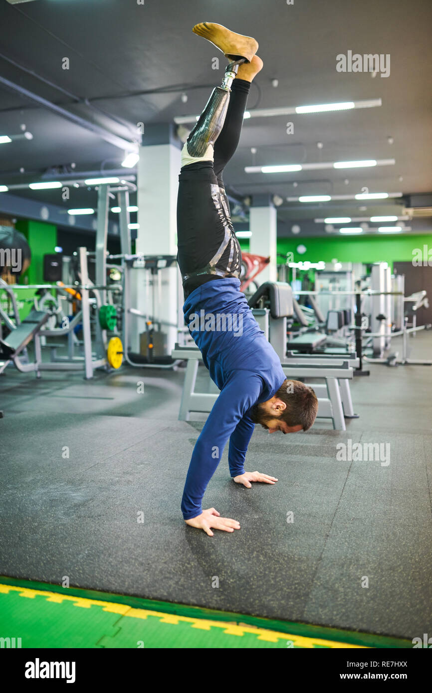 Strong skilled young bearded man  with prosthetic leg keeping balance while standing on hands in modern gym Stock Photo