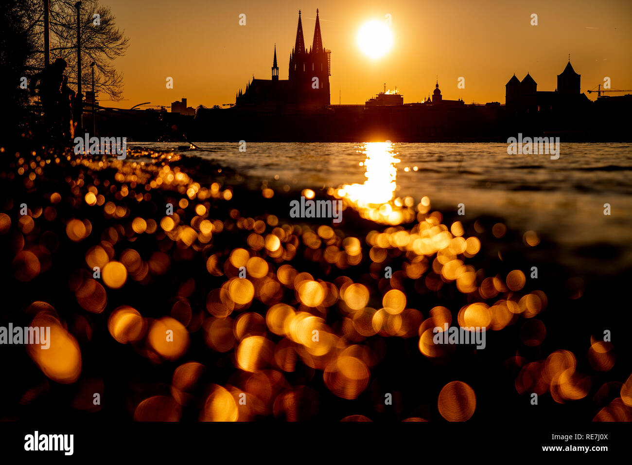 Die Sonne geht neben dem Kölner Dom unter. Im Vordergrund reflektiert das Wasser des Rheins. Stock Photo
