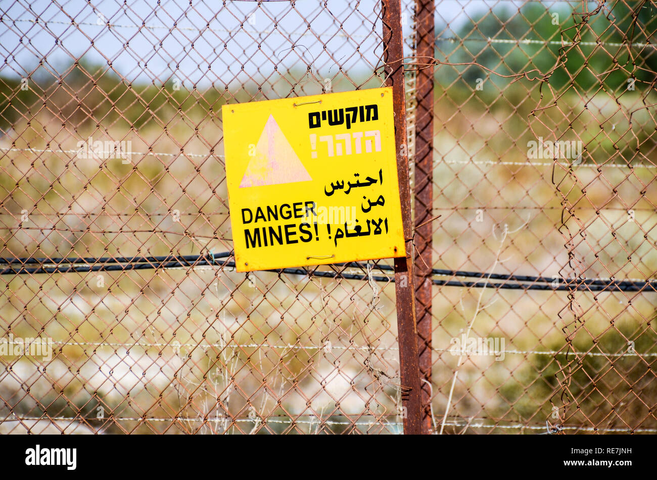 'Danger Mines' sign in Israel/West Bank Palestine, with barbed wires and disclaimer in Arabic and Hebrew, in front of an abandoned structure Stock Photo