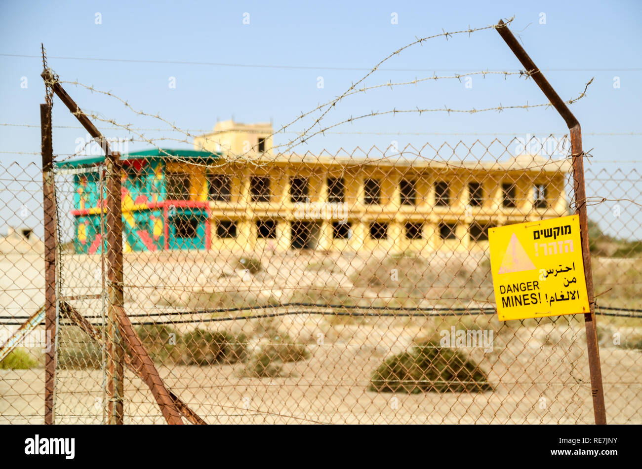 'Danger Mines' sign in Israel/West Bank Palestine, with barbed wires and disclaimer in Arabic and Hebrew, in front of an abandoned structure Stock Photo