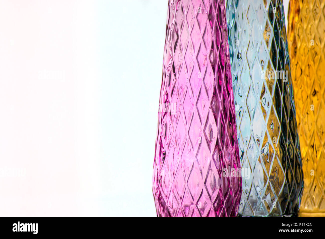 Three vases of colored glass with a pattern, close-up, isolated on a light background. Stock Photo