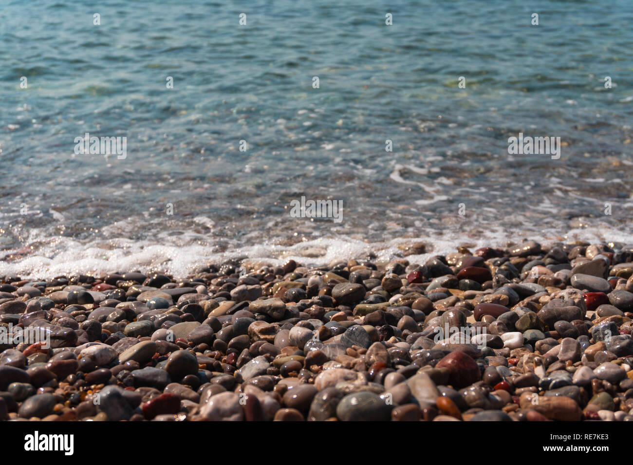 Colorful sea pebbles on the shore and clear water Stock Photo - Alamy