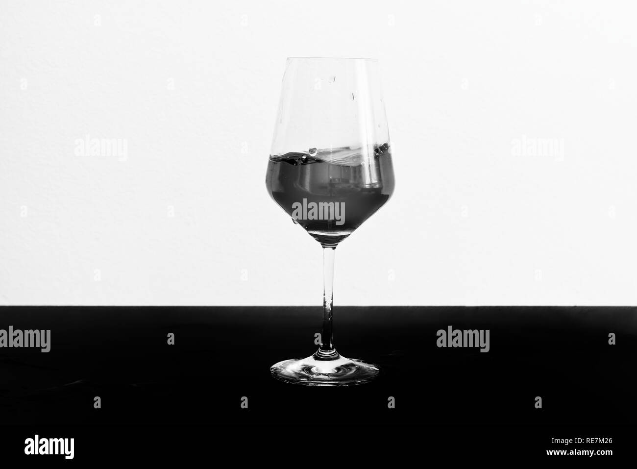 Black and white photo of red wine in motion in a glass on dark table and white background Stock Photo
