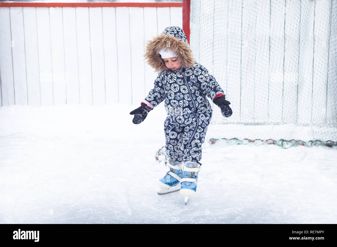 Child kid enjoy learning ice skating on skating rink overcome difficulties in a snowing park during winter holidays Stock Photo