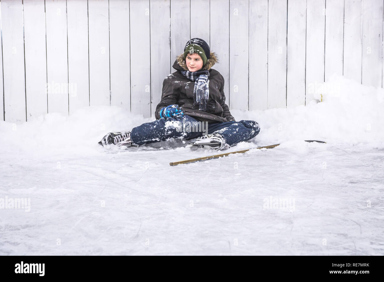 Kid boy hockey player having a rest on ice after playing hockey period on street skating rink during winter holidays Stock Photo