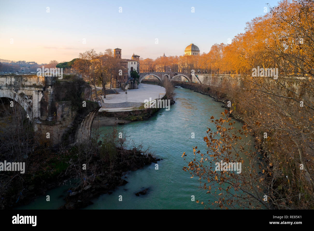 Rome, Italy, 12/29/2008: Rome's Tiberina island, Tiber river, river quay with yellow-leaved trees, in the background the dome of the synagogue Stock Photo