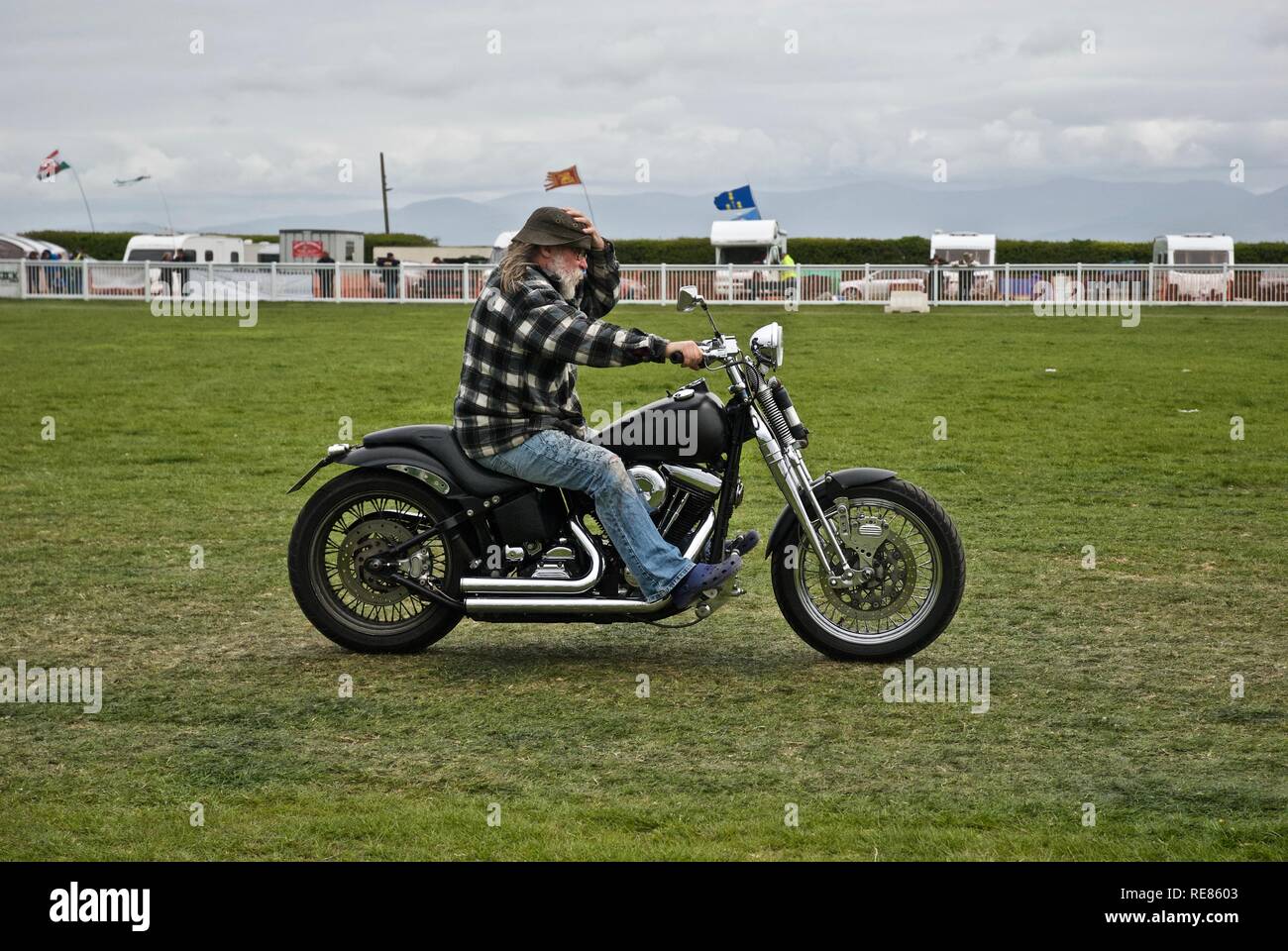 Man with a white beard holds onto his hat as he rides his Harley Davidson low rider bike at the Anglesey Vintage rally May 2010 Anglesey, Wales, UK Stock Photo