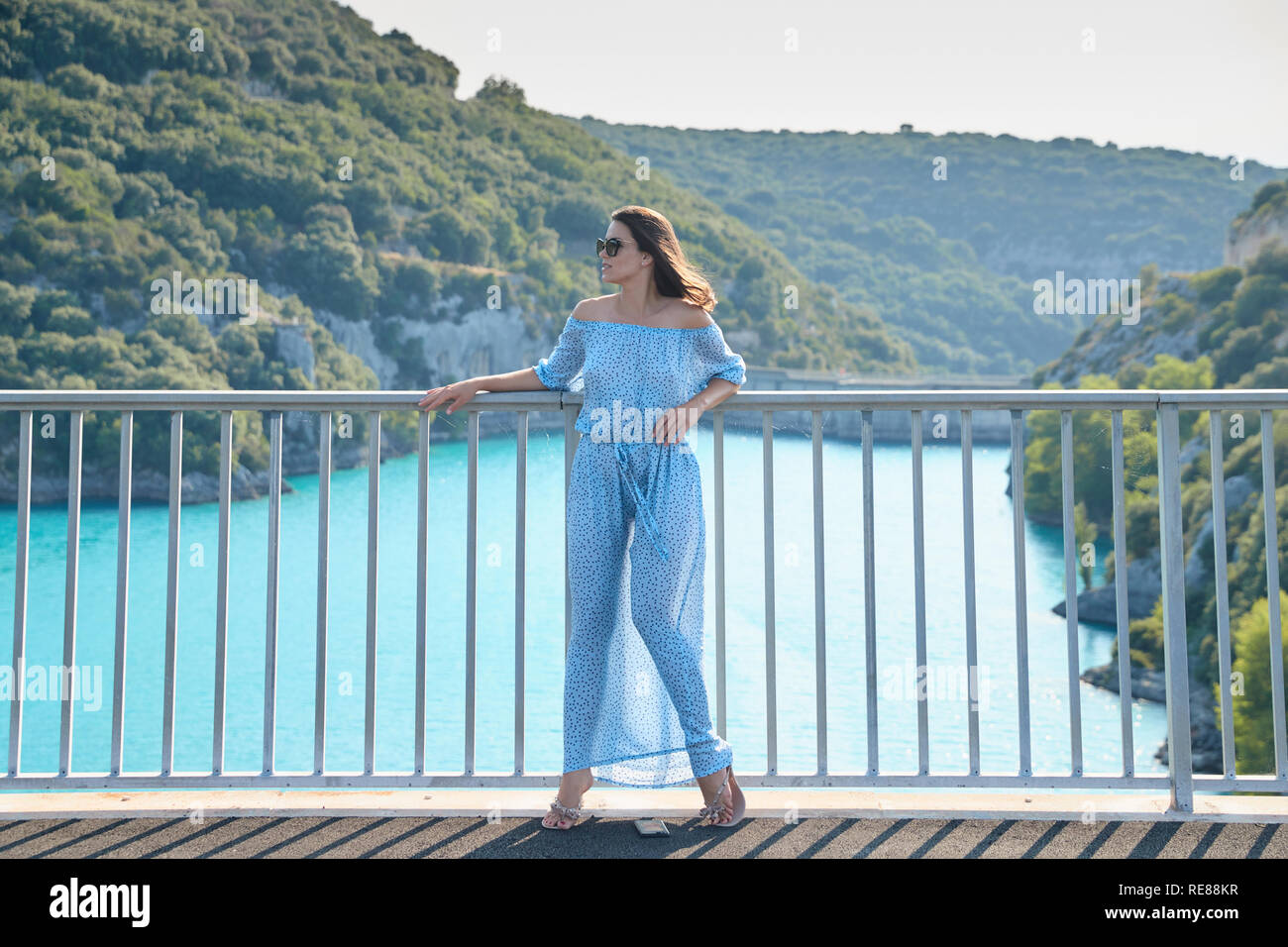 The beautiful girl in a blue dress and sunglasses poses on the bridge ...