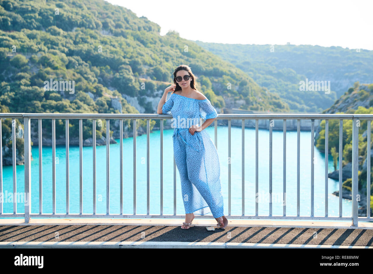 The beautiful girl in a blue dress and sunglasses poses on the bridge ...