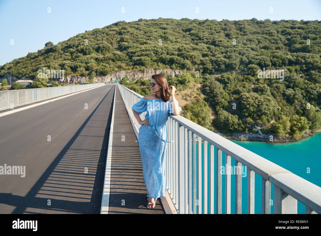 The beautiful girl in a blue dress and sunglasses poses on the bridge ...