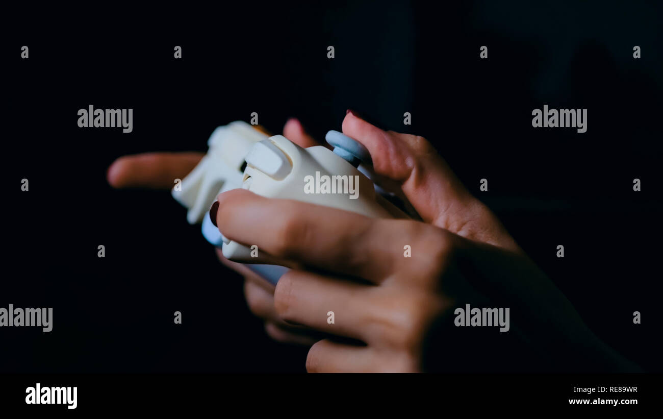 Young female gamer with gamepad or joystick playing video game in dark room. Gaming, fun, leisure time and entertainment concept Stock Photo