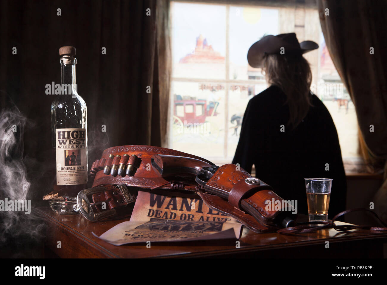 Gunslinger with gun belt and whisky looking out of window Stock Photo