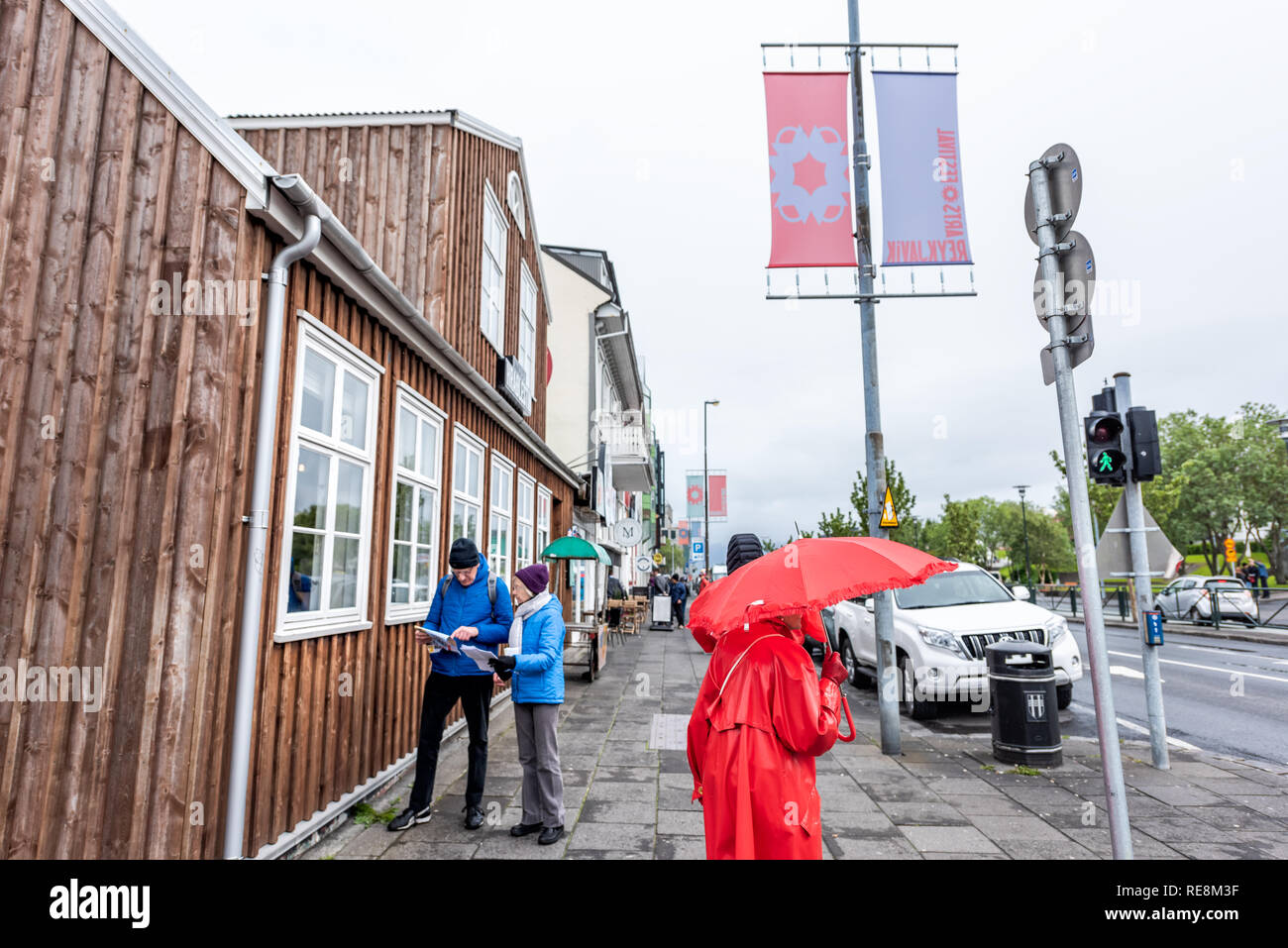 Reykjavik, Iceland - June 19, 2018: People tourists walking on street with red umbrella checking map directions on sidewalk in downtown center Stock Photo